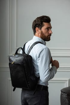 A fashionable man stands with a bag in a contemporary room, embodying urban style and professionalism.