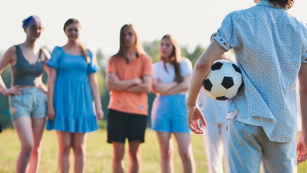 Young man is holding a soccer ball behind his back while his friends are waiting for the game to begin