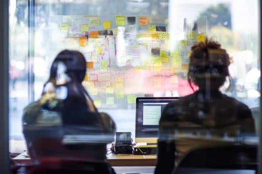 A team in a modern office setting collaborates as they face a wall of colorful notes, showcasing teamwork and creativity.