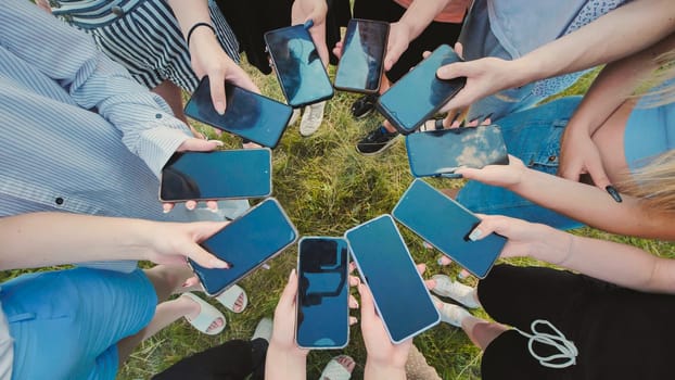 Group of young people standing in a circle on the grass showing their smartphone screens