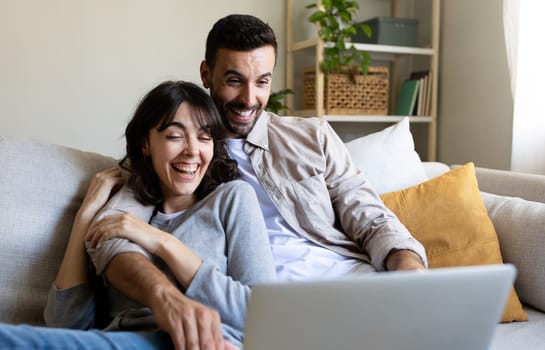 Caucasian couple laughing together watching comedy show on laptop sitting on the couch. Lifestyle and technology.