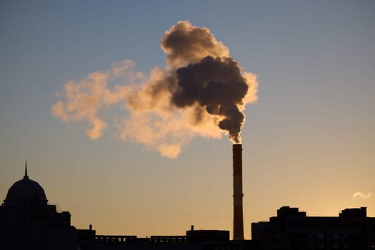 A silhouette of a chimney stands out against a colorful sunset, emphasizing urban life and industrial pollution