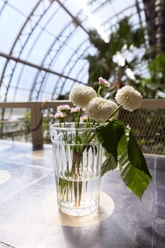 A charming glass vase filled with an abundance of soft white flowers and vibrant, lush greenery all around