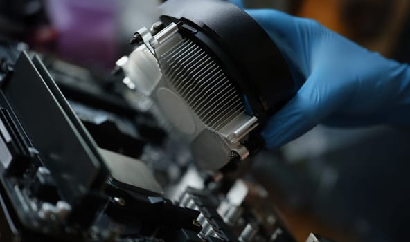 A hand in a glove installs a new cooler for a pc, close-up. Cooling system in the computer, repair, upgrade, cleaning from dust