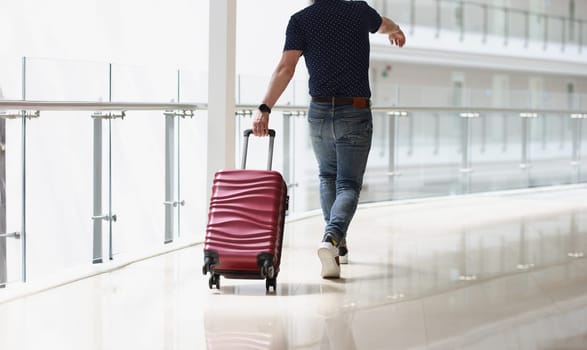 A man carrying a suitcase at the airport terminal, close-up, rear view. Travel, arrival at the station, passenger luggage