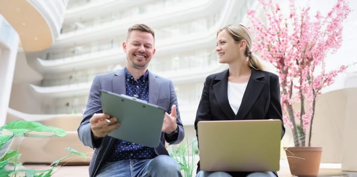 Happy man and woman with laptop and documents are sitting in the lobby of the business center, close-up. The joy of working together
