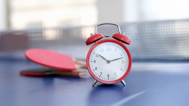 Red alarm clock on a tennis table, close-up, blurry. Office ping pong during the break. Sports recreation for employees
