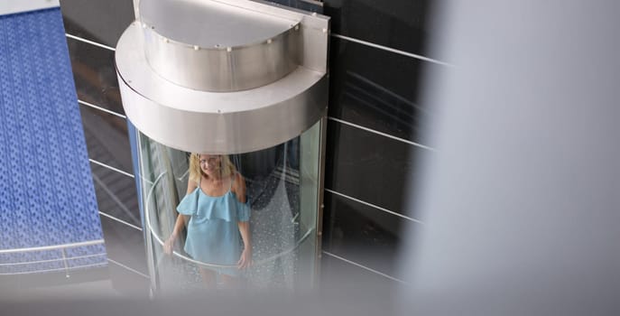 Beautiful woman in the glass elevator of the building, close-up, top view. Panoramic outdoor passenger lift