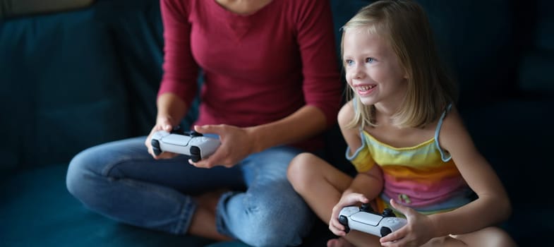 A little girl with a nanny sits on the couch plays a video game, close-up, blurry. Addiction to electronic games, leisure time during a pandemic