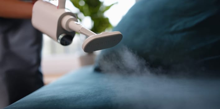 Steam comes out of the washing vacuum cleaner above the sofa, close-up, blurry. Hygienic reading of upholstered furniture
