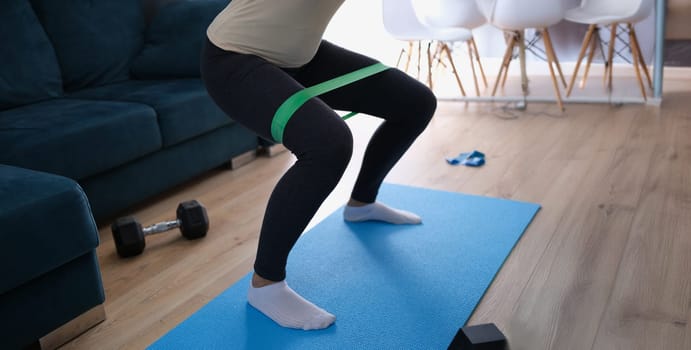 Woman doing exercises with elastic tape on her legs, close-up. Fitness at home, sports equipment for weight loss