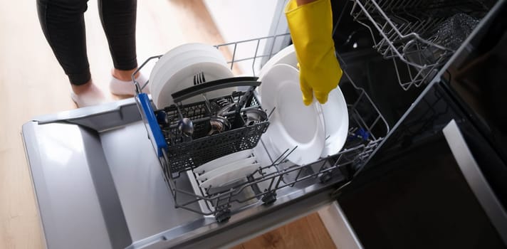 A woman takes out clean dishes from the dishwasher, close-up. Cutlery washing, household appliances, housework