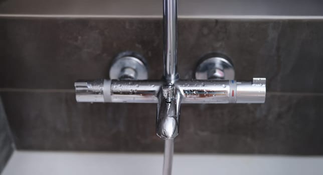 Water drops on the wall mixer in the bathroom, close-up. Chrome faucet on gray background. Plumbing