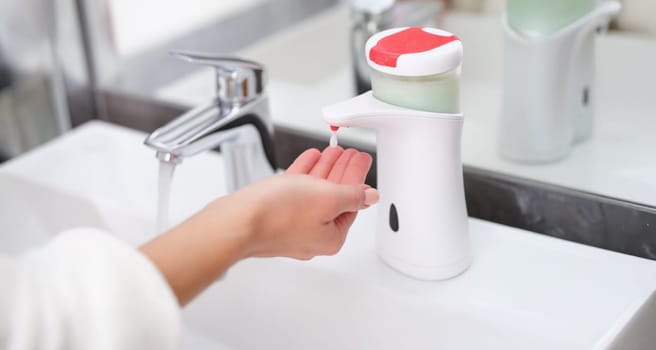 A drop of soap from a dispenser drips onto a woman's hand, close-up. Hand hygiene, bathroom. Washing