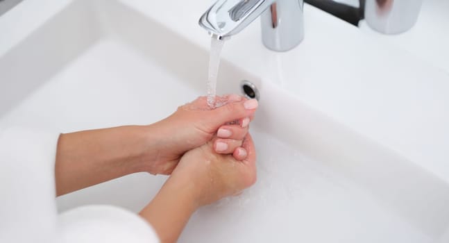 A woman washes her hands under the tap, close-up. Water pressure, plumbing. Hygiene, protection against germs