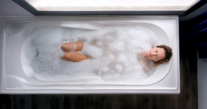 A woman lies in a soapy bath, top view. Relaxation, stress relief, body hygiene, aromatherapy. Beauty treatments, spa