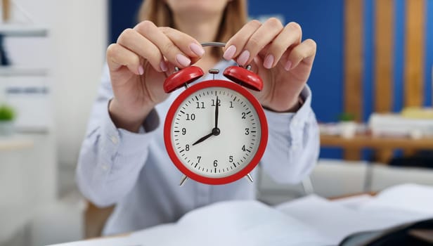 Woman holding a red alarm clock, close-up, blurry. Concept of day planning, meeting deadlines, productive morning