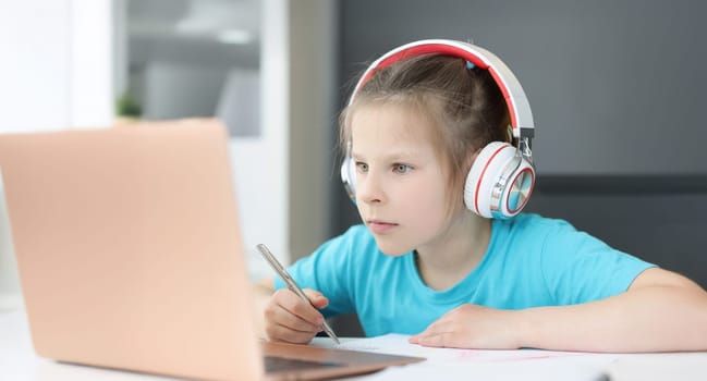 A girl in headphones looks attentively into a laptop, close-up. Distance learning during a pandemic, completing school assignments