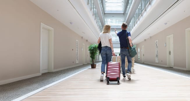 A man and a woman are walking with luggage along the hotel corridor, close-up, rear view. Accommodation in a resort complex