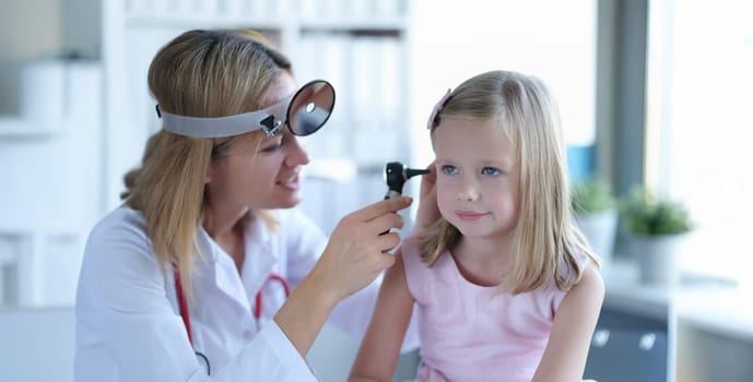 A woman otolaryngologist in a clinic looks at the ear of a little girl. Children's doctor, diagnosis of diseases, consultation
