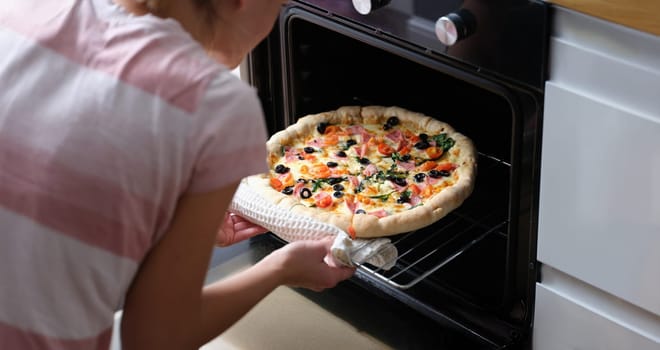 A woman takes homemade pizza with sausages out of the oven, close-up. Traditional Italian recipe, lockdown