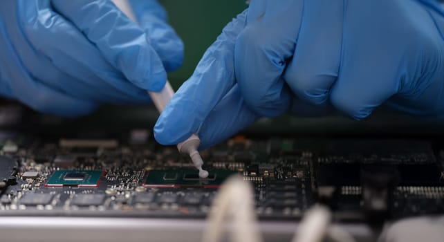 Gloved hands hold thermal paste on a laptop chip, close-up. Cleaning laptop from dust, service center