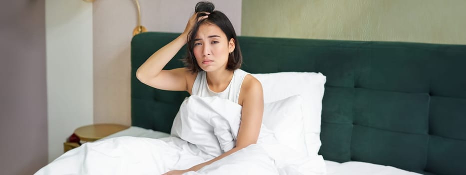 Portrait of sad young woman waking up, feeling bad, wants to sleep, wakes early morning, looking lazy and upset.