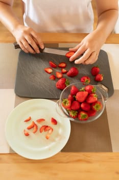 Close-up of fresh strawberries being sliced with a knife on a board in the kitchen.