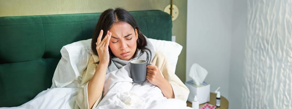 Flu, sickness and people. Young woman feeling sick, having fever and catching col, lying in bed with hot tea, taking drugs from influenza.