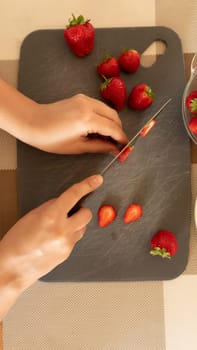 a woman's hands cut strawberries into slices.