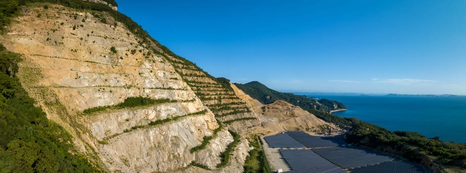 Terraced cut rock and stone at quarry above solar panels on coast. High quality photo