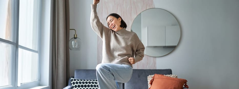 Portrait of happy asian woman dancing, rejoicing and triumphing, feeling upbeat at home. Copy space