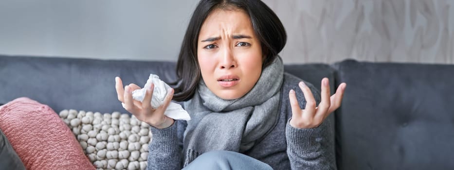 Portrait of sad woman feeling unwell, wearing warm clothes and scarf at her home without heating, staying on sick leave in her house.