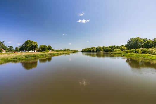 Beautiful landscape of long dirty river with green trees and bushes on both sides seen from bridge over water dam and water level