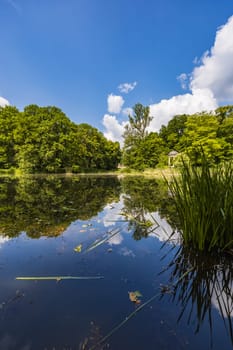 Beautiful and colorful park at sunny morning with blue sky with few clouds beautifully reflecting in big silent lake like in mirror