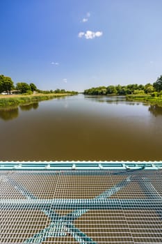 Beautiful landscape of long dirty river with green trees and bushes on both sides seen from bridge over water dam and water level