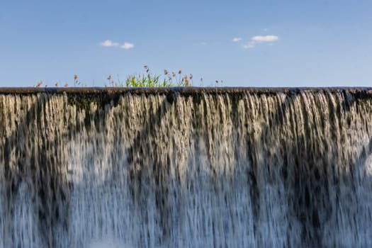 Small waterfall with streaming water over water level at water dam