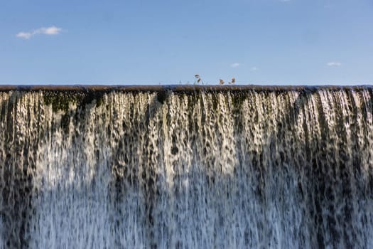 Small waterfall with streaming water over water level at water dam