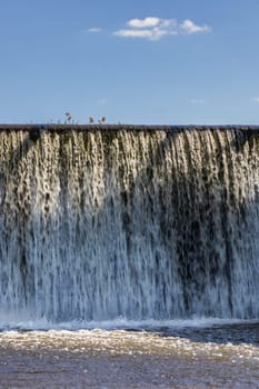 Small waterfall with streaming water over water level at water dam