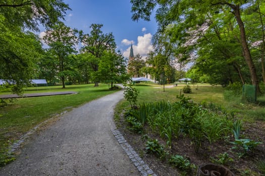 Long curvy path in beautiful green park with tower of building at sunny morning with blue sky and few white clouds