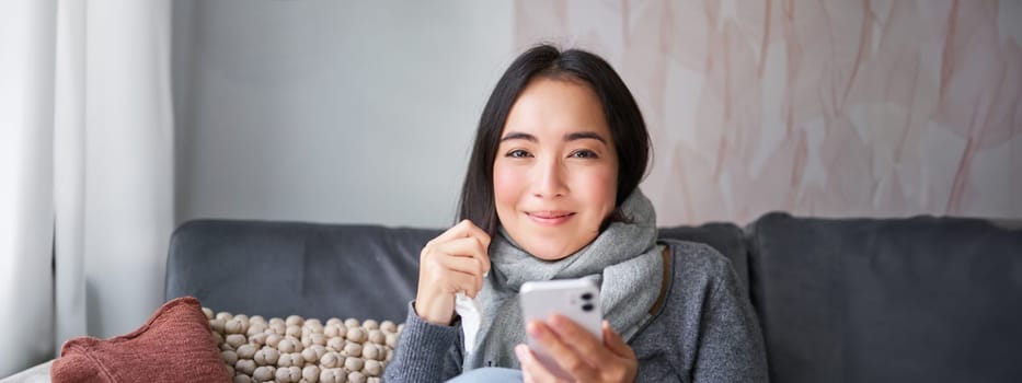 Portrait of korean woman feels sick, holding smartphone, calling doctor gp to get presctiption, caught cold, staying at home, using mobile phone.