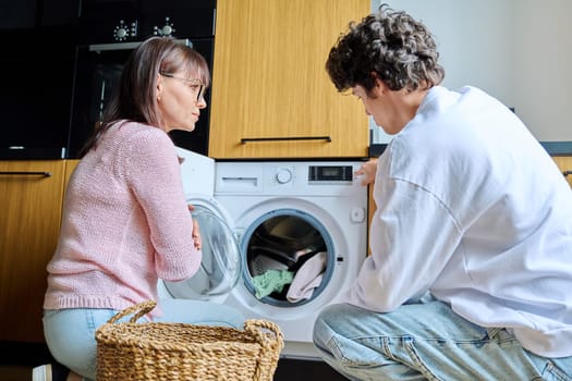 Family mother and teenage son together, at home near the washing machine, lifestyle, adolescence, communication, relationships, everyday domestic routine concept
