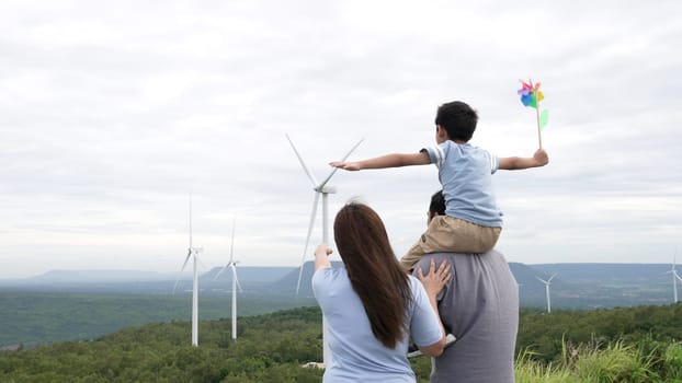 Concept of progressive happy family enjoying their time at the wind turbine farm. Electric generator from wind by wind turbine generator on the country side with hill and mountain on the horizon.