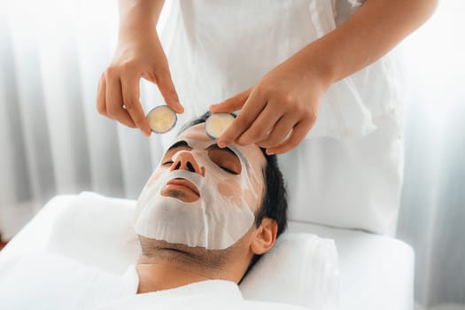 Serene daylight ambiance of spa salon, man customer indulges in rejuvenating with luxurious cucumber facial mask. Facial skincare treatment and beauty care concept. Quiescent