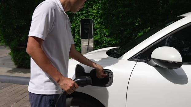 Progressive man install power cable plug to his electric vehicle, EV car from home charging station. Electric car driven by clean and renewable energy to preserve environment. Eco-friendly automobile.