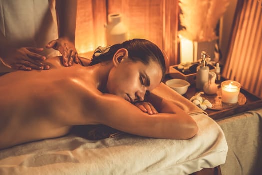 Caucasian woman customer enjoying relaxing anti-stress spa massage and pampering with beauty skin recreation leisure in warm candle lighting ambient salon spa at luxury resort or hotel. Quiescent