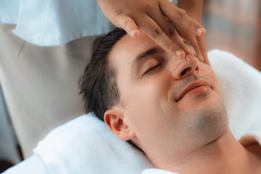 Caucasian man enjoying relaxing anti-stress head massage and pampering facial beauty skin recreation leisure in dayspa modern light ambient at luxury resort or hotel spa salon. Quiescent