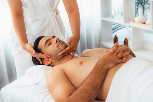 Caucasian man enjoying relaxing anti-stress head massage and pampering facial beauty skin recreation leisure in dayspa modern light ambient at luxury resort or hotel spa salon. Quiescent