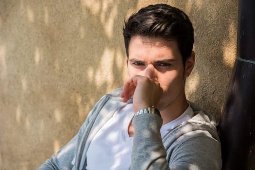 A man leaning against a wall with his hand on his nose. Photo of a man leaning against a wall, holding his nose in apparent discomfort