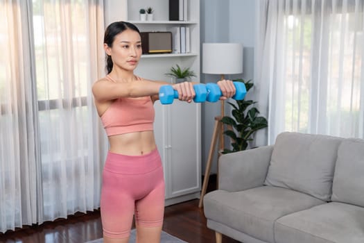 Vigorous energetic woman doing yoga with dumbbell weight lifting exercise at home. Young athletic asian woman strength and endurance training session as home workout routine.